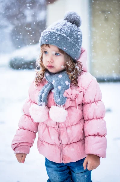 Söt baby flicka i rosa jackan och grå hatt njuter första snö b — Stockfoto