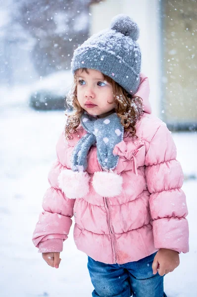 Söt baby flicka i rosa jackan och grå hatt njuter första snö b — Stockfoto