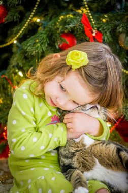 Şirin Bebek kız yeşil giysili Noel ağacının yakınında bir kedi öpüşme