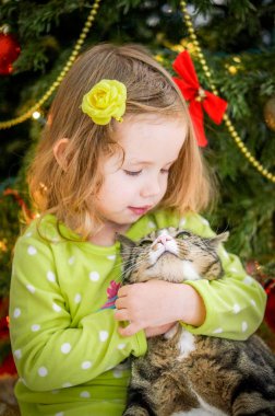 Şirin Bebek kız yeşil giysili Noel ağacının yakınında bir kedi öpüşme