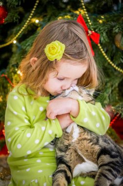 Şirin Bebek kız yeşil giysili Noel ağacının yakınında bir kedi öpüşme