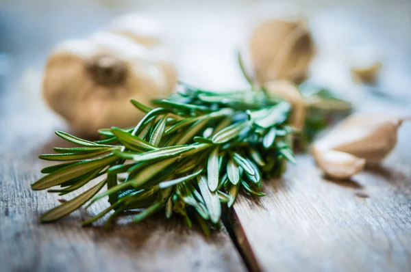 Fresh rosemary with fresh garlic on wooden background — Stock Photo, Image