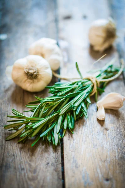 Fresh rosemary with fresh garlic on wooden background — Stock Photo, Image