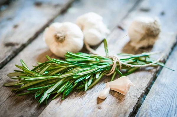 Fresh rosemary with fresh garlic on wooden background — Stock Photo, Image