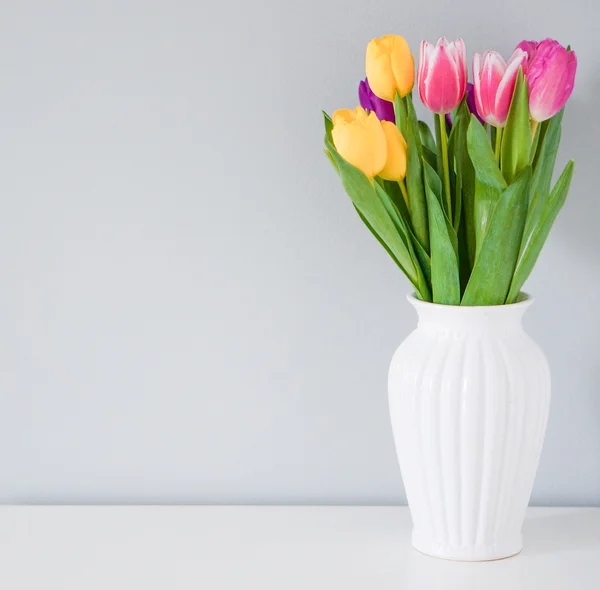 Bunte Tulpen in weißer Vase auf dem Tisch auf hellgrauem Hintergrund — Stockfoto