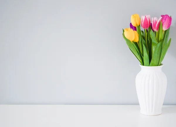 Coloridos tulipanes en jarrón blanco sobre la mesa sobre fondo gris claro — Foto de Stock