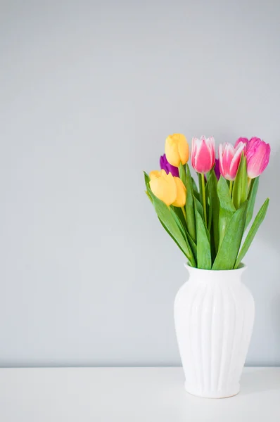 Kleurrijke tulpen in witte vaas op tafel op licht grijs backgro — Stockfoto