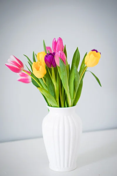 Coloridos tulipanes en jarrón blanco sobre la mesa sobre fondo gris claro — Foto de Stock