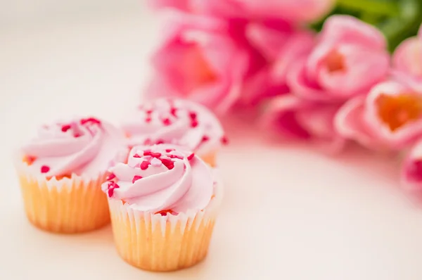 Cupcake con crema rosa, spruzzi di cuore e tulipani sul tavolo bianco — Foto Stock