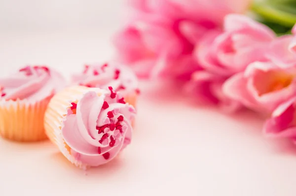 Gâteaux à la crème rose, saupoudrées de cœur et tulipes sur table blanche — Photo