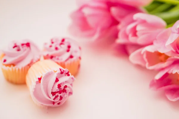 Cupcake con crema rosa, spruzzi di cuore e tulipani sul tavolo bianco — Foto Stock