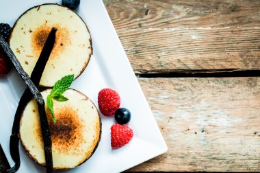 Creme brulee vanilya çubukları ve ahşap zemin üzerinde çilek ile