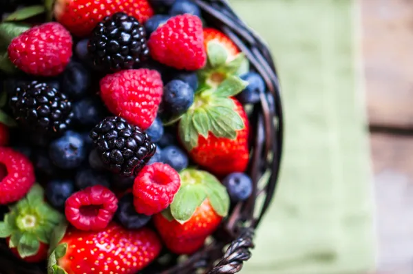 Mix of fresh berries in a basket on rustic wooden background — Stock Photo, Image