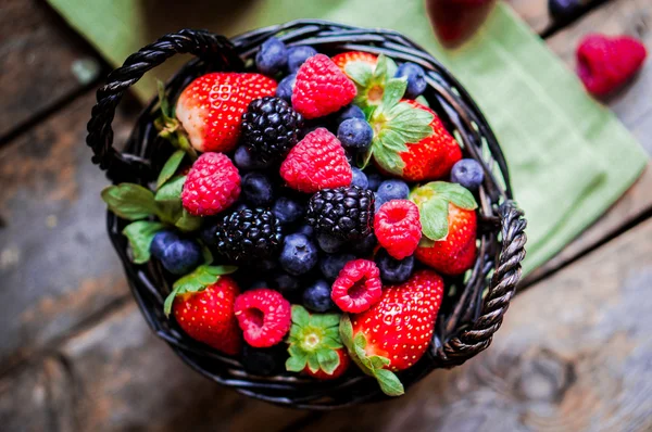 Mischung aus frischen Beeren in einem Korb auf rustikalem Holzgrund — Stockfoto