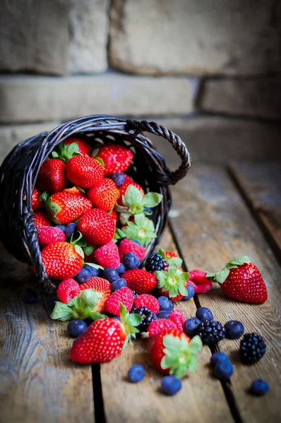 Mischung aus frischen Beeren in einem Korb auf rustikalem Holzgrund — Stockfoto