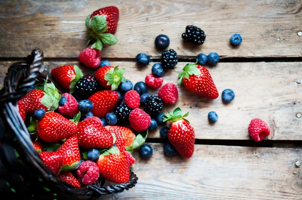 Mischung aus frischen Beeren in einem Korb auf rustikalem Holzgrund — Stockfoto