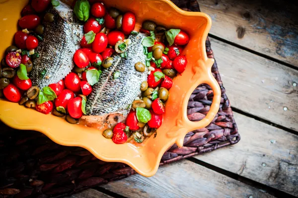 Baked seabass with tomatoes and basil on rustic wooden background — Stock Photo, Image