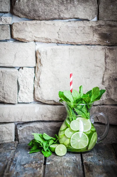 Water met limoenen (lemmetjes) en mint op houten achtergrond — Stockfoto