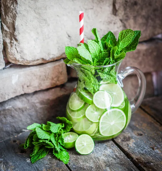 Water met limoenen (lemmetjes) en mint op houten achtergrond — Stockfoto