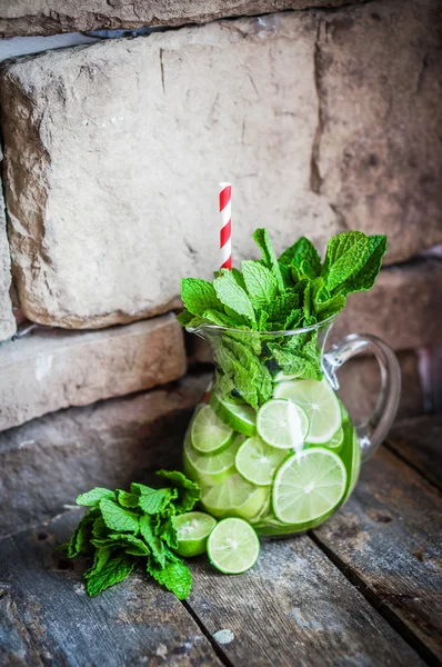 Water with limes and mint on wooden background — Stock Photo, Image