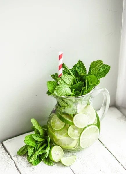 Water met limoenen (lemmetjes) en mint op houten achtergrond — Stockfoto