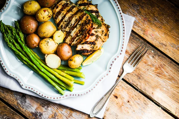 Pollo a la parrilla con patatas y espárragos sobre fondo de madera — Foto de Stock