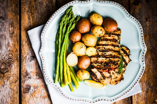 Grilled chicken with potatoes and asparagus on wooden background — Stock Photo, Image