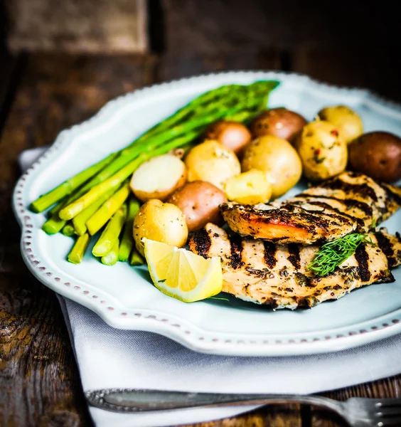 Grilled chicken with potatoes and asparagus on wooden background — Stock Photo, Image