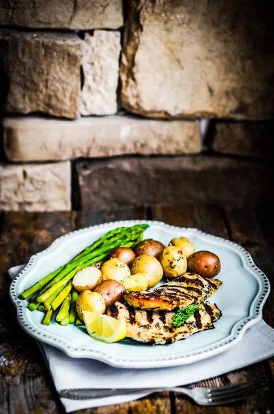 Grilled chicken with potatoes and asparagus on wooden background — Stock Photo, Image