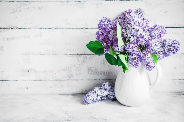 Lilacs in white vase on rustic background — Stock Photo, Image