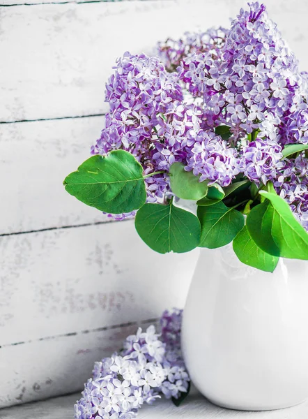 Lilacs in white vase on rustic background — Stock Photo, Image