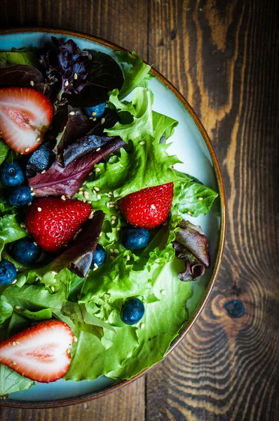 Salada verde com bagas no fundo de madeira — Fotografia de Stock