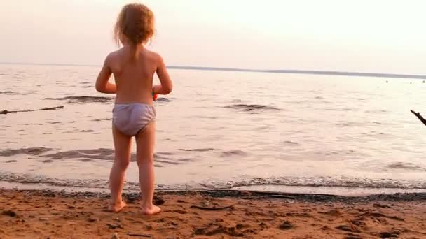 Little girl plays, looks afar at water — Stock Video