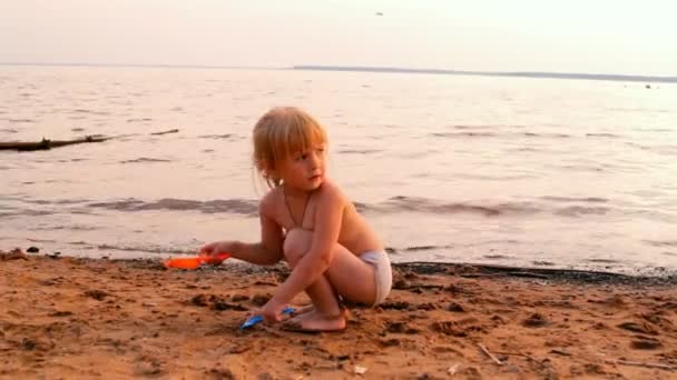 Little girl plays, looks afar at water — Stock Video