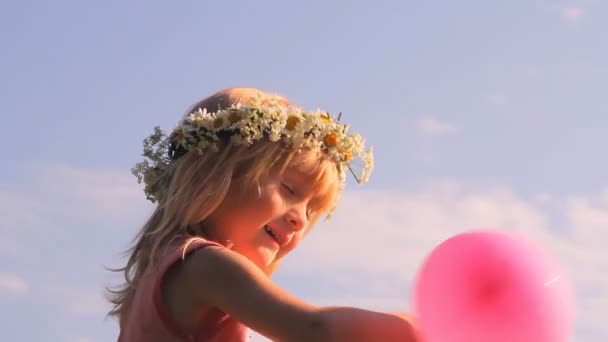 Das Mädchen im Kranz aus Kamillenblüten spielt mit einem Ball — Stockvideo