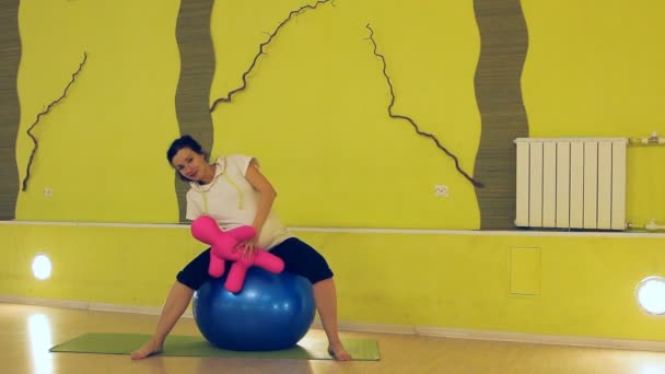 Een zwangere vrouw met een pop doen oefeningen met de bal, yoga — Stockvideo