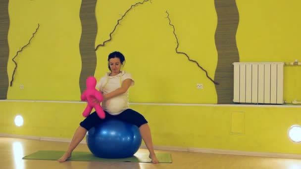 Seorang wanita hamil dengan boneka melakukan latihan dengan bola, yoga — Stok Video