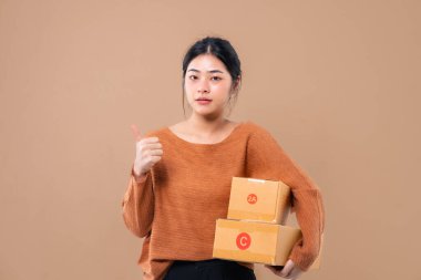 Teslimat kuryesi ve nakliye hizmeti konsepti. Kahverengi ekran arka planında izole edilmiş paket kutuları tutan mutlu Asyalı kadın. 