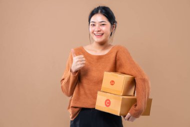 Teslimat kuryesi ve nakliye hizmeti konsepti. Kahverengi ekran arka planında izole edilmiş paket kutuları tutan mutlu Asyalı kadın. 