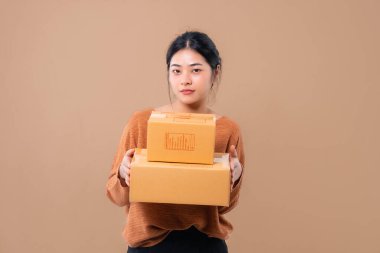 Teslimat kuryesi ve nakliye hizmeti konsepti. Kahverengi ekran arka planında izole edilmiş paket kutuları tutan mutlu Asyalı kadın. 