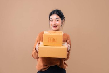 Teslimat kuryesi ve nakliye hizmeti konsepti. Kahverengi ekran arka planında izole edilmiş paket kutuları tutan mutlu Asyalı kadın. 