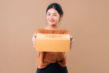 Teslimat kuryesi ve nakliye hizmeti konsepti. Kahverengi ekran arka planında izole edilmiş paket kutuları tutan mutlu Asyalı kadın. 