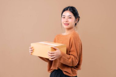 Teslimat kuryesi ve nakliye hizmeti konsepti. Kahverengi ekran arka planında izole edilmiş paket kutuları tutan mutlu Asyalı kadın. 