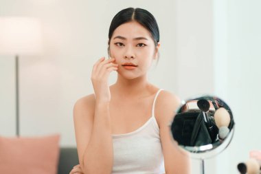 Gülümseyen güzel Asyalı kadının yakından çekilmiş portresi. Aynaya bakıyor. Cildine dokunuyor.. 