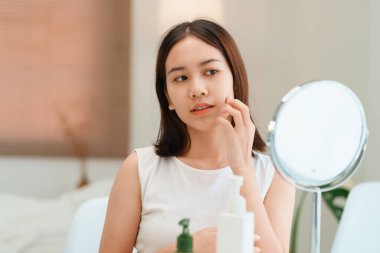 Gülümseyen güzel Asyalı kadının yakından çekilmiş portresi. Aynaya bakıyor. Cildine dokunuyor.. 