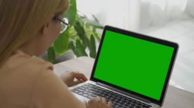 Ofiste çalışan bir iş kadınının omuz üstü fotoğrafı. Masanın üstünde, yeşil ekrana bakıyor. Laptop yeşil ekranlı dizüstü bilgisayar kullanan kişi.
