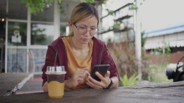 Genç Asyalı kadın kafeteryada buzlu çay içip arkadaşlarıyla sohbet ediyor. Kahve dükkanında cep telefonu kullanan kız..