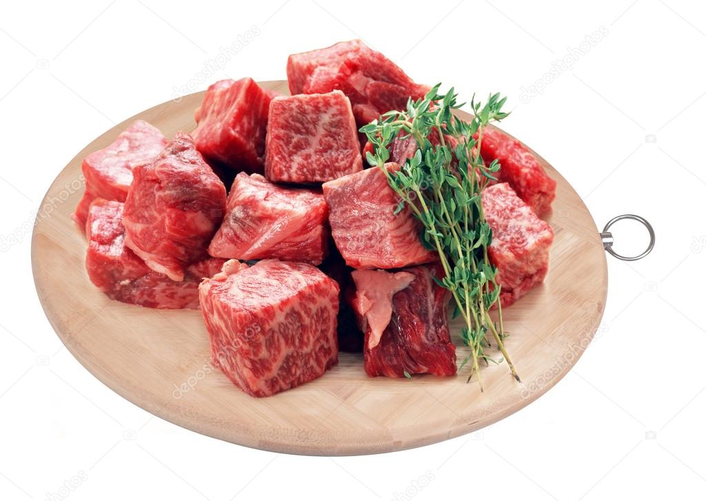 Raw fresh beef cubes on board with greens on white background