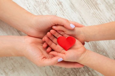 Kırmızı kalp, çocuk ve annenin elleri tahta arka planda. Sağlık ve aile kavramı.