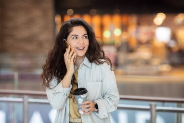 Genç ponpon kız akıllı telefon kullanıyor ve kahve içiyor kağıt bardakta. Kafede şık bir kadın..